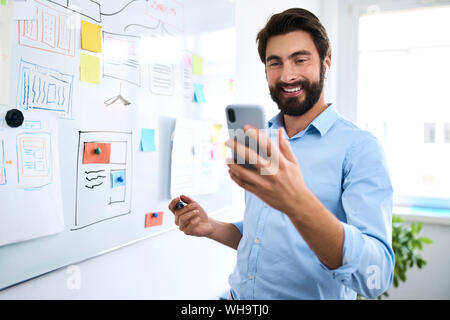 Businessman standing in front of a whiteboard and using his smartphone Stock Photo