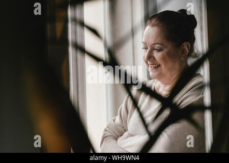 Happy senior woman looking out of window at home Stock Photo