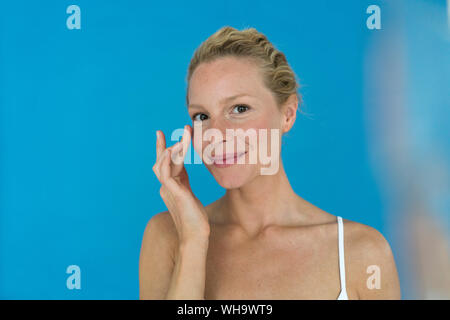 Portrait of beautiful blond woman applying eye cream Stock Photo