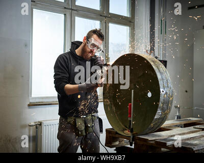 Man working on metal container with grinder Stock Photo