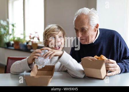 Happy grandfather and grandson eating burger together at home Stock Photo