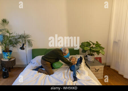 Happy grandfather playing with grandson on bed at home Stock Photo