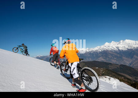 Mountain bikers cycle along a snow covered slope in the Himalayas with views of the Langtang range in the distance, Nepal, Asia Stock Photo