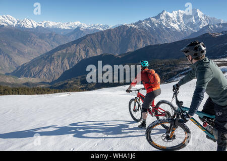 Mountain bikers descend a snow covered slope in the Himalayas with views of the Langtang range in the distance, Nepal, Asia Stock Photo