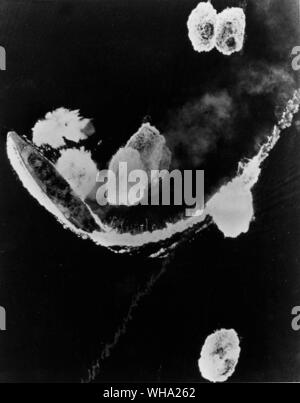 WW2: Japanese ships under attack from US carrier planes in Kure Bay, Monshu Island. Taken by planes from the USS Hornet (CV-12). A Japanese battleship of the Yamato class wheels to avoid bombs. March 19th 1945. Stock Photo