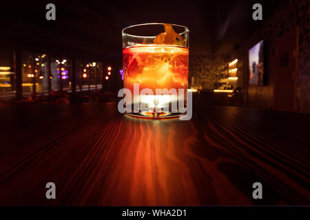 Colorful alcohol cocktail with a warm backlight on a wooden table. Served with ice and orange peel. Boulvardier or Negroni. Frozen glass. Stock Photo