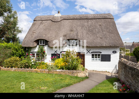 The delightful, thatched Church Cottage in a corner of the churchyard at Bishop's Cleeve, Gloucestershire UK Stock Photo