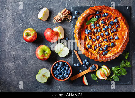 Apple Blueberry Pie on a black slate tray on a concrete table with ingredients, horizontal view from above, flatlay, close-up, free space for text Stock Photo