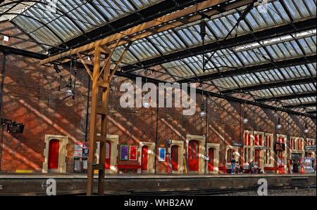 Strong summer sun creates shadows across the big brick wall and doors as passengers wait for a northbound train at Stoke on Trent railway on 23.8.19. Stock Photo