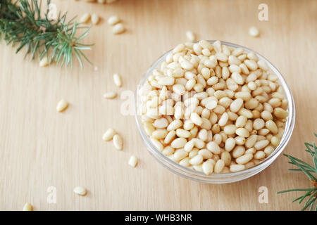 Cedar pine nuts in glass bowl with cedar brunches on wooden background Stock Photo