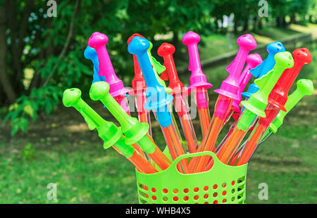 Toy soap bubbles in the shape of a sword stand in a green basket on a natural background. Stock Photo