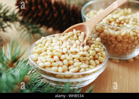Cedar pine nuts in glass bowls with cones, spoon, cedar brunch on wooden background Stock Photo