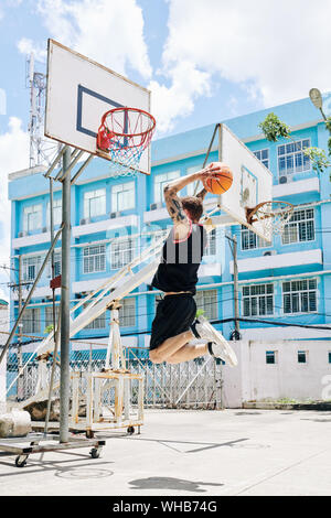 Basketball player in uniform jumping high to throw ball in basket when he is playing on street court Stock Photo