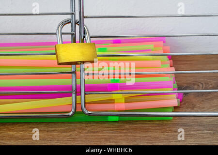 A lot of multicolored plastic cocktail tubes closed in a cage locked with padlock. Stop using disposable drinking straws concept. Front view. Stock Photo