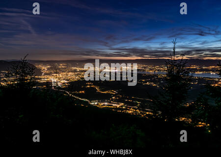 Evening top view of city lights, French Annemasse, Swiss Geneva,lake Geneva and picturesque sky with dark clouds after sunset,photo with long exposure. Stock Photo