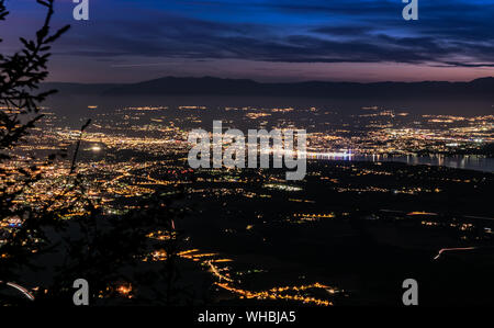 Evening top view of city lights, French Annemasse, Swiss Geneva,lake Geneva and picturesque sky with dark clouds after sunset,photo with long exposure. Stock Photo