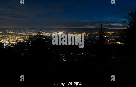 Evening top view of city lights, French Annemasse, Swiss Geneva,lake Geneva and picturesque sky with dark clouds after sunset,photo with long exposure. Stock Photo