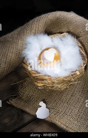 Empty Broken Big Golden Egg in birds nest over rustic wooden background close-up, vertical orientation, rustic style. Success Symbol or Happy Easter C Stock Photo