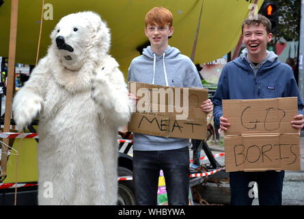 A person in a polar bear suit on Deansgate with young men holding ironic messages: 'I Love Meat' and 'Go Boris'. Northern Rebellion protesters, part of the global movement Extinction Rebellion, marched through Manchester, uk, and held a series of die-ins to urge for action on climate change on September 2nd, 2019. Protest sites included Barclays Bank, a Primark store and HSBC Bank. This was the fourth day of a protest which blocked Deansgate, a main road in central Manchester. Stock Photo