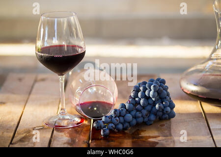 Glass of red wine with purple grapes. Dropped wine glass and spilled red wine on a wooden table as a symbol of fail, slight unpleasantness Stock Photo