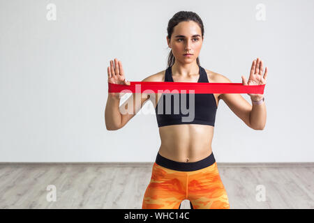 Portrait of young sporty woman wearing black top and orange leggings performs exercises for the muscles of the hands, workout with resistance band on Stock Photo