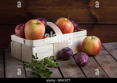 Gifts of autumn: apples and plums in a basket on a wooden background Stock Photo