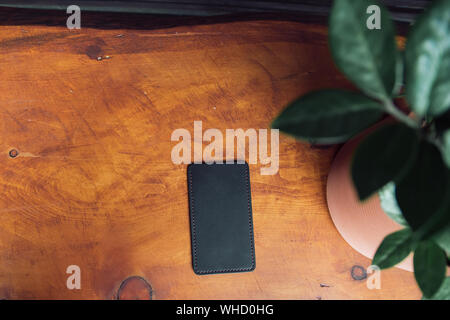 Manly leather phone case on wooden background. Next to the aksusekar is a potted flower. Stock Photo