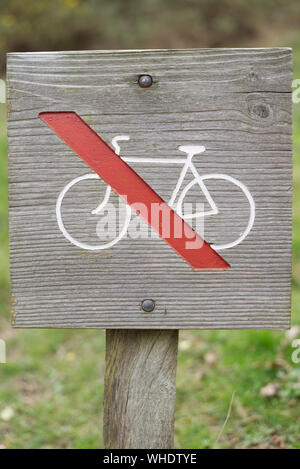 Wooden No cycling sign with red line through white bicycle symbol on wooden post with green bokeh background Stock Photo