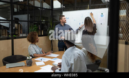 Two diverse business speakers give presentation drawing on whiteboard Stock Photo