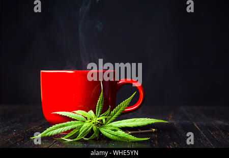 Cup of tea with marijuana cannabis leaves on dark background Stock Photo