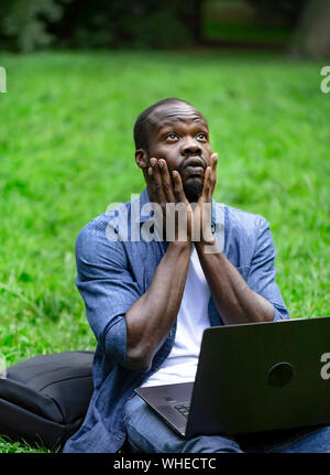 Thoughtful black student looking for inspiration looking upwards while working at laptop outdoors Stock Photo