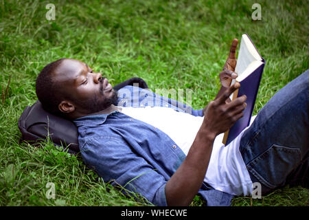 Concentrated black male student reading a textbook lying on a campus lawn Stock Photo