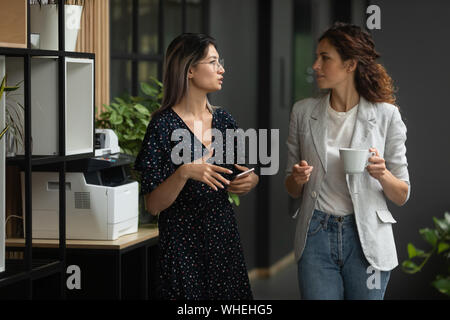 Serious diverse female colleagues talking walking in office space Stock Photo