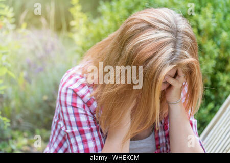 Attractive long haired young woman holding her hands over her head and looking down. She is depressed. Stock Photo