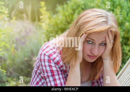 Attractive young woman holding her hand over her head and looking at the camera. She is depressed and thinking about how to solve problem Stock Photo