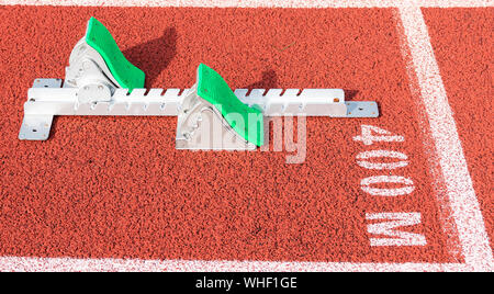 A set of track and field sprinters starting blocks are set up at the 400 meter starting line on a red track. Stock Photo