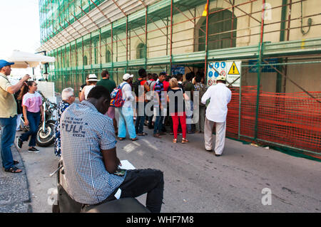 Men and women of many ethnicities wait outside the Immigration office, Ortigia, Sicily, Italy. Lineups, long delays are everyday sights. Processing. Stock Photo