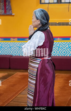 A devout Buddhist woman stops for prayer & meditation upon entering a temple. In Elmhurst, Queens, New York City. Stock Photo