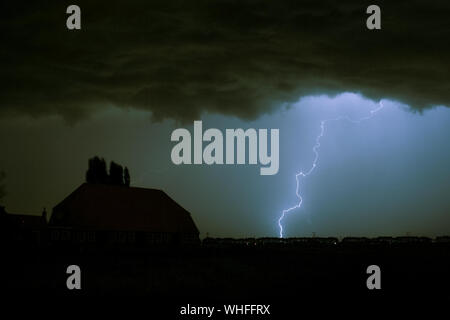 Lightning strike on a dark blue sky over a house silhouette. Stock Photo