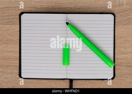 Green marker and opened notebook on desk Stock Photo