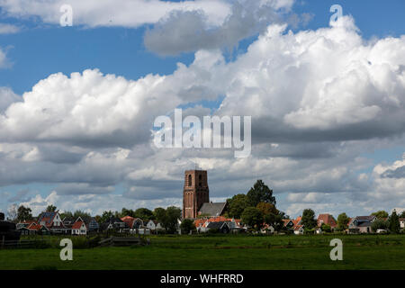 Small village of Ransdorp near Amsterdam rising from the agrarian green pasture fields with dramatic clouds in the blue sky above Stock Photo