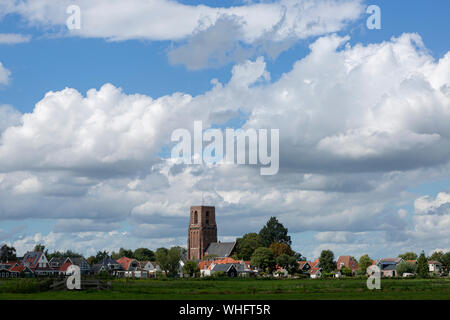 Small village of Ransdorp near Amsterdam rising from the agrarian green pasture fields with dramatic clouds in the blue sky above Stock Photo