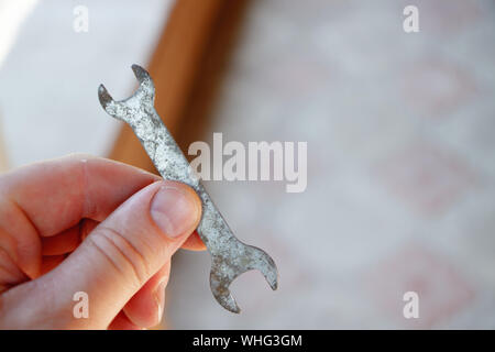 Male hand holds small old rusty double open end wrench lies on tiled floor in sun glare Stock Photo