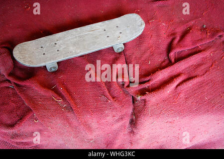 Old vintage wooden skateboard on dirty red surface, selective focus Stock Photo