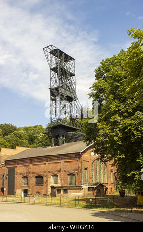 The mine tower for black coal mining Landek in city Ostrava in the Czech Republic. In the background is blue sky with white clouds. Forests are trees Stock Photo