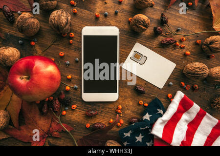Mobile phone and SIM card with Thanksgiving day autumn arrangement. Top view flat lay of smartphone device with blank mock up screen as copy space. Stock Photo