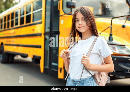 Cute girl wearing bag standing near bus going to school posing to camera pensive close-up Stock Photo