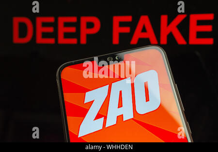ZAO app logo on the smartphone and red words DEEP FAKE on the background screen. Zao is currently a number one AI face swap entertaining app in China. Stock Photo