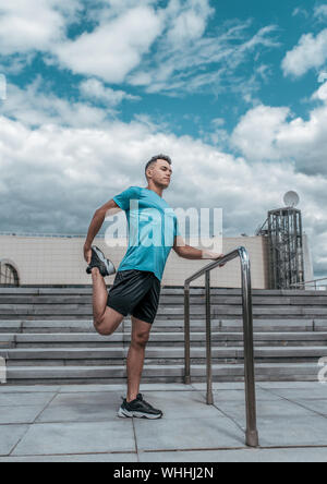 Athlete guy doing knee and leg muscle stretch before training. In the summer in the city, preparing for a jogging fitness workout, sportswear shorts t Stock Photo