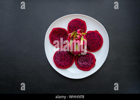 Red whole dragon fruit and slices on a white plate isolated on black background for border design with copy space for text Stock Photo